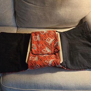 May include: A fabric lap desk featuring a central tray with a removable cushion cover. The cover displays an orange and black tiger stripe pattern with the Cincinnati Bengals logo and text. The side flaps are solid black fabric.