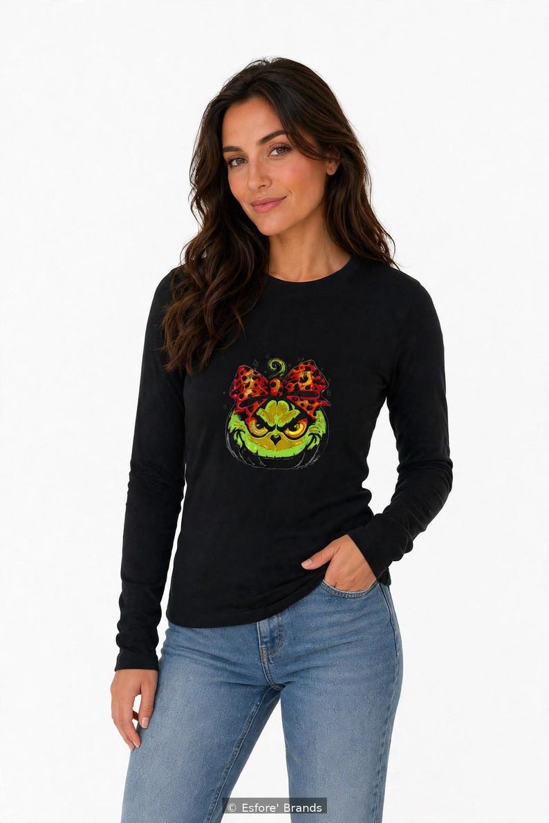 Puede incluir: Una camiseta negra de manga larga con un estampado gr&aacute;fico de un rostro verde y ce&ntilde;udo que recuerda a una calabaza, adornado con un lazo de estampado de leopardo en tonos rojos y negros.