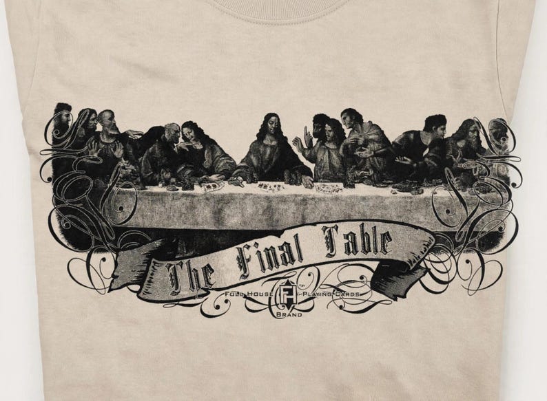 May include: A beige t-shirt featuring a black graphic print of a group of people seated at a long table. Below the table is a banner with the text "The Final Table" and "Full House Playing Cards Brand" with decorative flourishes.