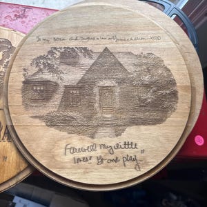 May include: A round wooden plaque featuring a laser-engraved illustration of a house. The text at the top reads "To my sons and daughters in law and grandchildren XOXO" and the bottom text reads "Farewell my little ones! Go and play."