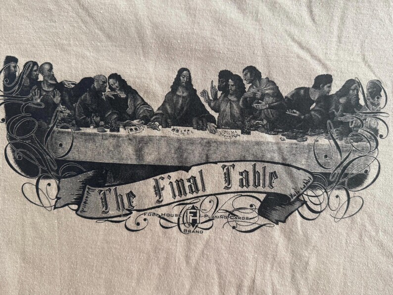 May include: A beige t-shirt featuring a black graphic print of a group of people seated at a long table. Below the table is a banner with the text The Final Table and the logo for Faded House Playing Cards brand.
