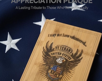 Pode incluir: Uma placa retangular de bambu com um emblema de águia gravado e um escudo, o texto "I may not have volunteered..." no topo e "but I'm DAMN proud to be a VET!" na parte inferior, centrada sobre um tecido azul escuro com estrelas brancas.