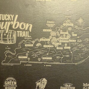 Op de afbeelding: Een kaart van de Kentucky Bourbon Trail, met een gedetailleerde omtrek van de staat en gemarkeerde distilleerderijen. Het ontwerp bevat de tekst "Kentucky Bourbon Trail" en een vatillustratie, allemaal in een lichte kleur op een donkere achtergrond.