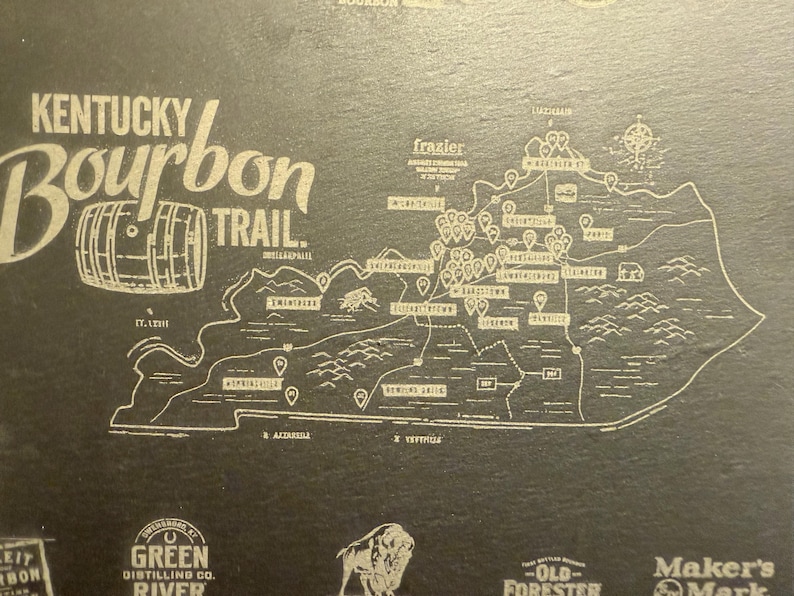 Op de afbeelding: Een kaart van de Kentucky Bourbon Trail, met een gedetailleerde omtrek van de staat en gemarkeerde distilleerderijen. Het ontwerp bevat de tekst "Kentucky Bourbon Trail" en een vatillustratie, allemaal in een lichte kleur op een donkere achtergrond.