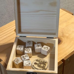 May include: A light-colored wooden box with a hinged lid and metal latch containing seven wooden dice and one circular wooden token. Each die features a unique icon and number. The token displays a barrel graphic and the text SKIP A STEP.