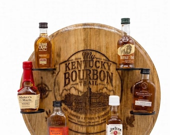 Pode incluir: Um expositor circular de madeira feito com uma tampa de barril e gravado com o texto My Kentucky Bourbon Trail. O suporte contém seis garrafas miniatura de bourbon, incluindo Elijah Craig, Buffalo Trace, Maker's Mark, Bulleit, Jim Beam e Woodford Reserve.