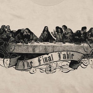 May include: A beige t-shirt featuring a black graphic print of a group of people seated at a long table. Below the table is a banner with the text "The Final Table" and "Full House Playing Cards Brand" with decorative flourishes.