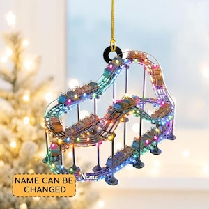 May include: A decorative roller coaster ornament with colorful LED lights. The ornament features a miniature roller coaster track with several cars. The text "NAME CAN BE CHANGED" is visible on a yellow rectangle.
