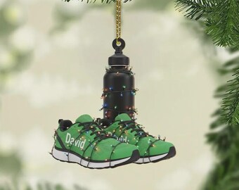 May include: A Christmas ornament featuring a black water bottle and a pair of green running shoes. The shoes have the name "David" on them. The ornament is decorated with a string of colorful lights and hangs from a gold chain.