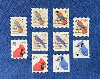 May include: A collection of nine vintage US postage stamps featuring various birds, including a cardinal, bluebird, and American Kestrel. The stamps are in good condition and have a variety of denominations, including 1 cent, 3 cents, 20 cents, and 30 cents.