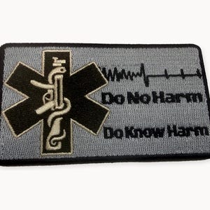 May include: A rectangular embroidered patch with a grey background and black border. It features a black Star of Life symbol with a white snake and staff, a black EKG line, and the black embroidered text Do No Harm and Do Know Harm.