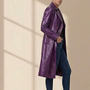 Peut inclure: Un long manteau violet à double boutonnage avec un motif texturé en relief façon crocodile, un col à revers et des manches longues. Le manteau est porté sur un haut noir, un jean bleu foncé et des bottines en cuir noir à élastique latéral.