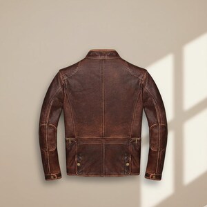 May include: A brown leather jacket with a distressed finish. The jacket features a classic collar, shoulder panels, and multiple pockets with button and buckle details. The back view showcases the tailored design and stitching.