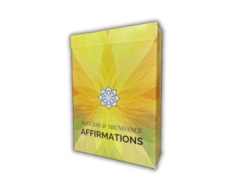 Puede incluir: Una caja amarilla y naranja con un diseño de flor blanca y el texto "Success & Abundance Affirmations".