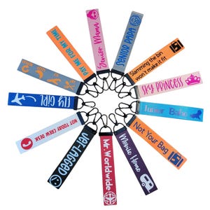 May include: A set of 12 colorful luggage tags with various phrases and designs. The tags are made of fabric and have a metal ring for attaching to luggage.