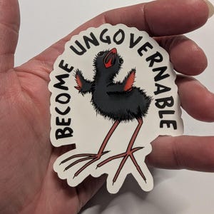 May include: A white sticker featuring a cartoon bird with black plumage, red wings and legs. The sticker has the text "I BECOME UNGOVERNABLE" in a semi-circular design around the bird. The bird has long, thin legs.