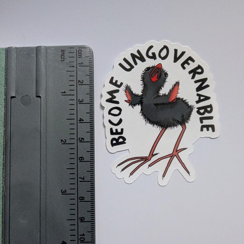 May include: A sticker featuring a black bird illustration with red accents and long legs. The sticker has the words "BECOME UNGOVERNABLE" in a semi-circle. The sticker is approximately 7.6 cm in height.