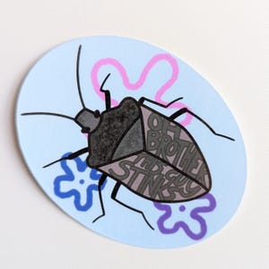 Puede incluir: Una obra de arte ovalada de color azul claro que representa un insecto estilizado con el texto "OH BROTHER THIS STINKS". El insecto es negro y gris, con detalles florales rosas y azules. Es probable que sea un objeto decorativo.