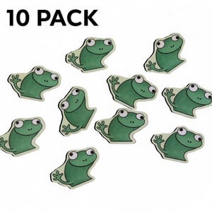 May include: A pack of ten green frog-shaped stickers. Each sticker features a cartoon frog with large eyes and a smiling expression. The stickers have a white border and are arranged on a white background. The text "10 PACK" is at the top.
