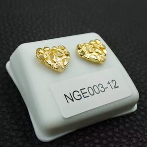 May include: Two gold heart-shaped earrings with a textured surface. The earrings are displayed on a white box with the text "NGE003-12".
