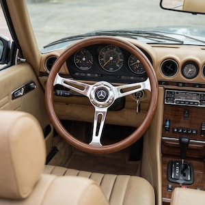Puede incluir: El interior de un vehículo con un volante de aro de madera, tres radios cromados y un emblema central de Mercedes-Benz. El salpicadero incluye indicadores analógicos, una radio Becker Grand Prix y detalles en madera. Asientos de cuero color beige.