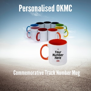 Puede incluir: Una taza de cerámica blanca con un borde y un asa naranja. La taza tiene un círculo blanco con el texto "Your Number Here" en negro. La taza está rodeada de otras tazas de varios colores. El texto "Commemorative Track Number Mug" está debajo de la taza.