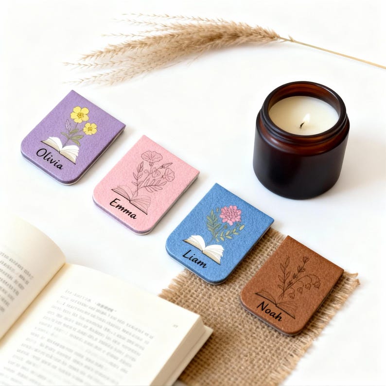 May include: Four personalised bookmarks in purple, pink, blue, and brown, each with a floral design and a name: Olivia, Emma, Liam, and Noah. A lit candle in a brown jar and an open book are also visible.