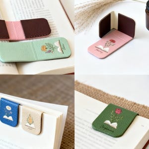 May include: A selection of leather bookmarks in shades of brown, pink, blue, and green. Some have floral designs and open book illustrations. The bookmarks are shown on open books, indicating their use as reading accessories.