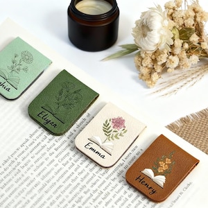 May include: Four leather magnetic bookmarks with floral designs and names: Sophia, Eligan, Emma, and Henry. Each bookmark features an open book illustration. Colours include green, cream, and brown.