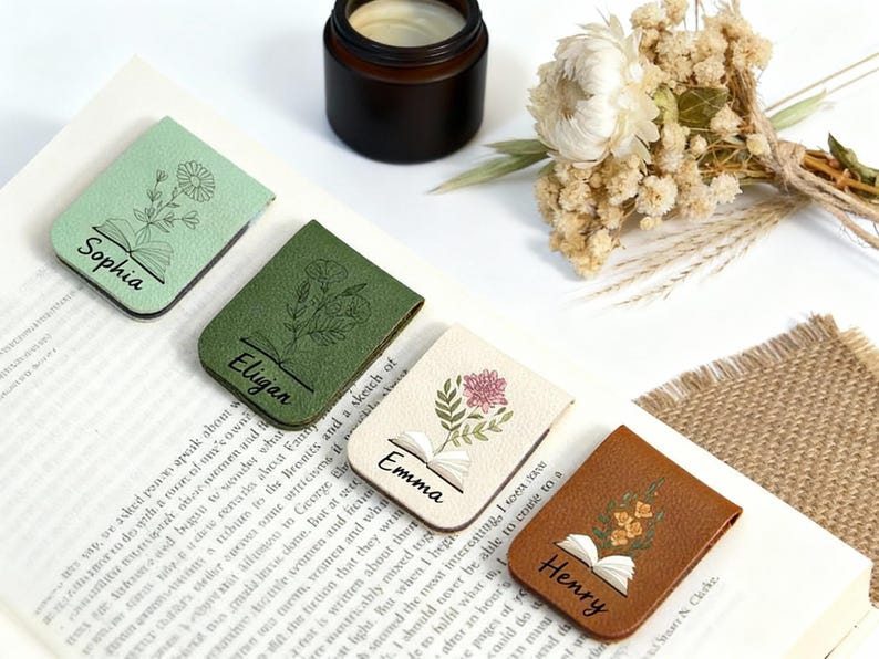 May include: Four leather magnetic bookmarks with floral designs and names: Sophia, Eligan, Emma, and Henry. Each bookmark features an open book illustration. Colours include green, cream, and brown.