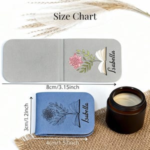 May include: Two personalised book-shaped bookmarks, one grey and one blue, each with a floral design and the name "Isabella." The grey bookmark is 8cm long, and the blue one is 4cm long. A small candle sits nearby.