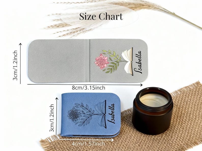 May include: Two personalised book-shaped bookmarks, one grey and one blue, each with a floral design and the name "Isabella." The grey bookmark is 8cm long, and the blue one is 4cm long. A small candle sits nearby.