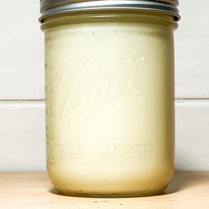 May include: A clear glass jar with a silver lid filled with a white substance. The jar has the word "Ball" and "Wide Mouth" printed on it.