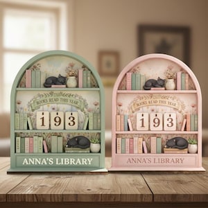 May include: Two decorative bookshelf-shaped book trackers, one mint green and one pink. Each features miniature books, a sleeping black cat, and the text "BOOKS READ THIS YEAR" above the number "193". The bottom reads "ANNA'S LIBRARY".