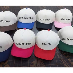 Może przedstawiać: Kolekcja czapek bejsbolowych z białymi koronami i kolorowymi daszkami. Daszki są dostępne w r&oacute;żnych kolorach, w tym brązowym, jasnoniebieskim, czarnym, r&oacute;żowym, granatowym, r&oacute;żowym, czerwonym i leśnozielonym. Każda czapka ma pasujący guzik na g&oacute;rze.