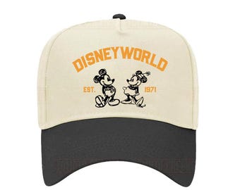 May include: A baseball cap with a cream-colored crown and a black brim. The front of the cap features the words "DISNEYWORLD" in orange, along with a black and white graphic of Mickey and Minnie Mouse, and the text "EST. 1971".