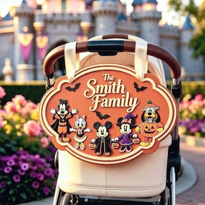 May include: An oval orange sign with the text The Smith Family, featuring cartoon characters in Halloween costumes including a vampire, a witch, and a pumpkin, attached to a beige stroller with cream-colored ribbons and a brown handle.