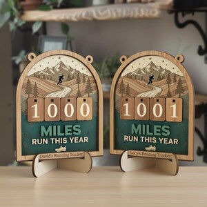 Op de afbeelding: Twee houten hardlooptellers met een berg- en hardloperontwerp. De trackers tonen "1000" en "1001" mijl gelopen dit jaar. De tekst "MILES RUN THIS YEAR" en een schoenafbeelding zijn ook inbegrepen.