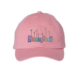 Pu&ograve; includere: Cappellino da baseball rosa con un logo Disneyland ricamato che presenta un castello colorato e bandiere.