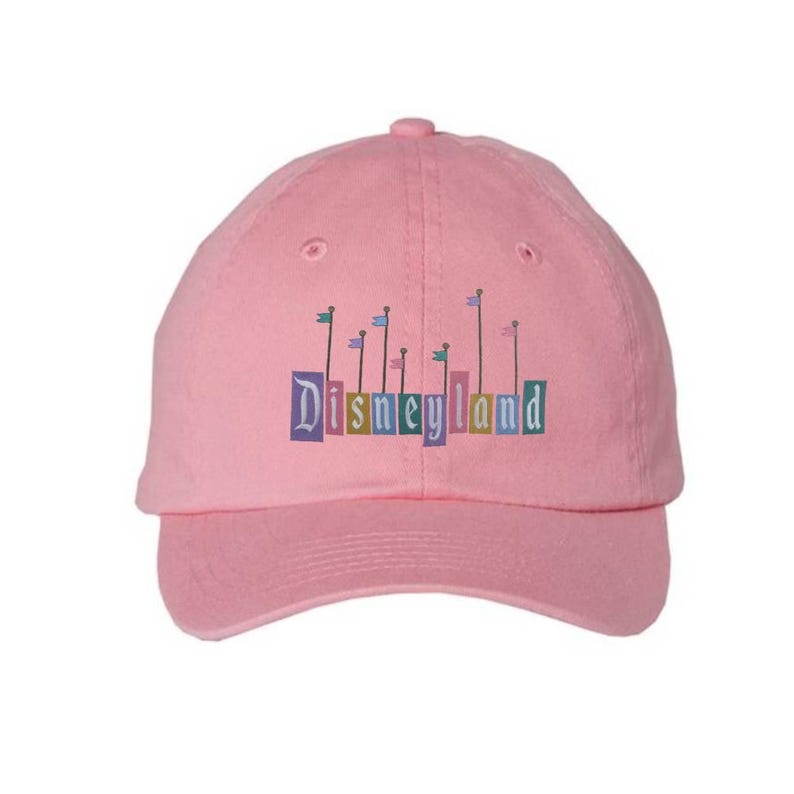 Pu&ograve; includere: Cappellino da baseball rosa con un logo Disneyland ricamato che presenta un castello colorato e bandiere.
