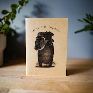 May include: A brown card with a black and white illustration of two bears. The text on the card reads "Never Stop Exploring."