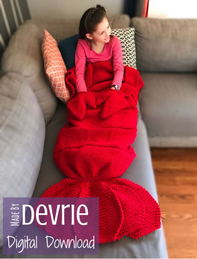 May include: A red knitted mermaid tail blanket with a girl sitting on a couch. The blanket is made with a textured stitch and has a large tail fin. The text "MADE BY Devrie Digital Download" is visible in the bottom left corner of the image.