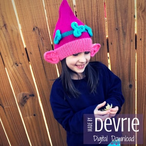 May include: A pink knitted hat with blue and pink felt flowers and ears. The hat is made for a child and has the text "Made by Devrie Digital Download" on the bottom right corner.