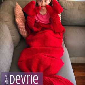 May include: A red knitted lobster tail blanket with a child wearing it. The blanket has large lobster claws attached to the top. The text "MADE BY Devrie Digital Download" is on the bottom of the image.