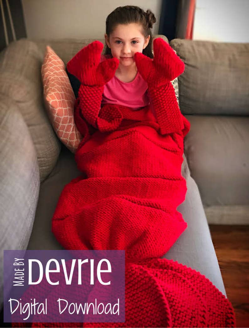 May include: A red knitted lobster tail blanket with a child wearing it. The blanket has large lobster claws attached to the top. The text "MADE BY Devrie Digital Download" is on the bottom of the image.