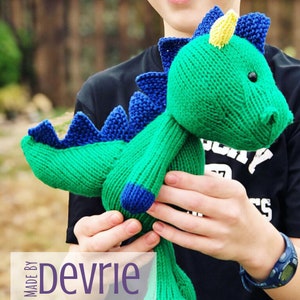 May include: A green knitted dragon toy with blue and yellow accents. The dragon is being held by a person. The text "MADE BY Devrie Digital Download" is visible in the image.