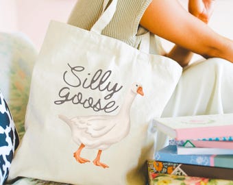May include: A white canvas tote bag with the text "Silly Goose" printed in black. A white goose with an orange beak is illustrated on the bag.