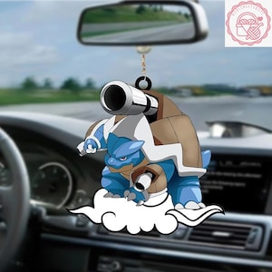 May include: A blue and brown cartoon character car charm. The charm features a blue turtle-like creature with cannons on its back, standing on a white cloud. The charm hangs from a black ring and is suspended in front of a car's interior.