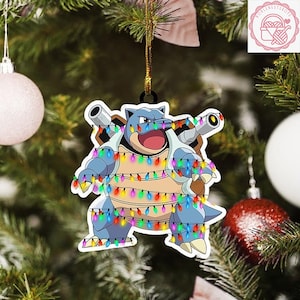May include: A blue and white cartoon character Christmas ornament, wrapped in colorful string lights, hangs from a gold string. The ornament is in front of a Christmas tree with other ornaments.