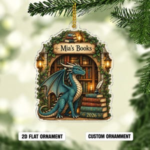 May include: A flat, arched acrylic ornament featuring a blue dragon sitting in a library with bookshelves, ivy, and lanterns. The text reads Mia's Books and 2026 on a stack of books. It includes a gold hanging cord for display on a tree branch.